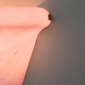 A close-up of a pink sculptural wall sconce casting a warm glow onto a textured gray wall.