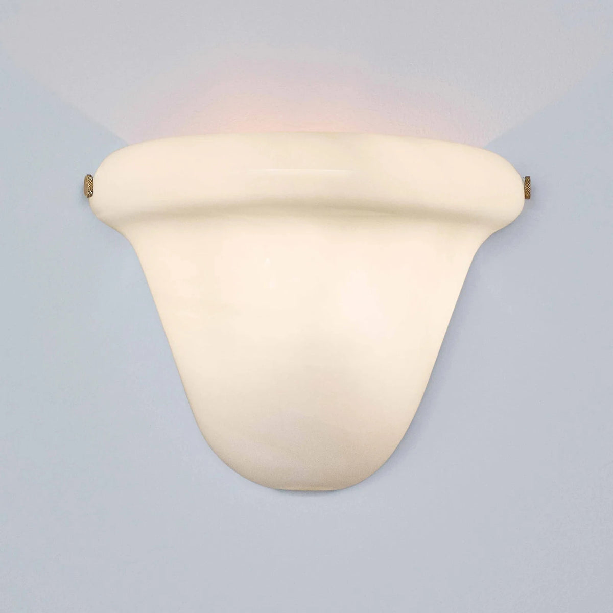 A modern wall-mounted sconce with a curved, shield-like shade in a warm cream or off-white finish, casting a soft warm light upward and downward against a pale blue-gray background.