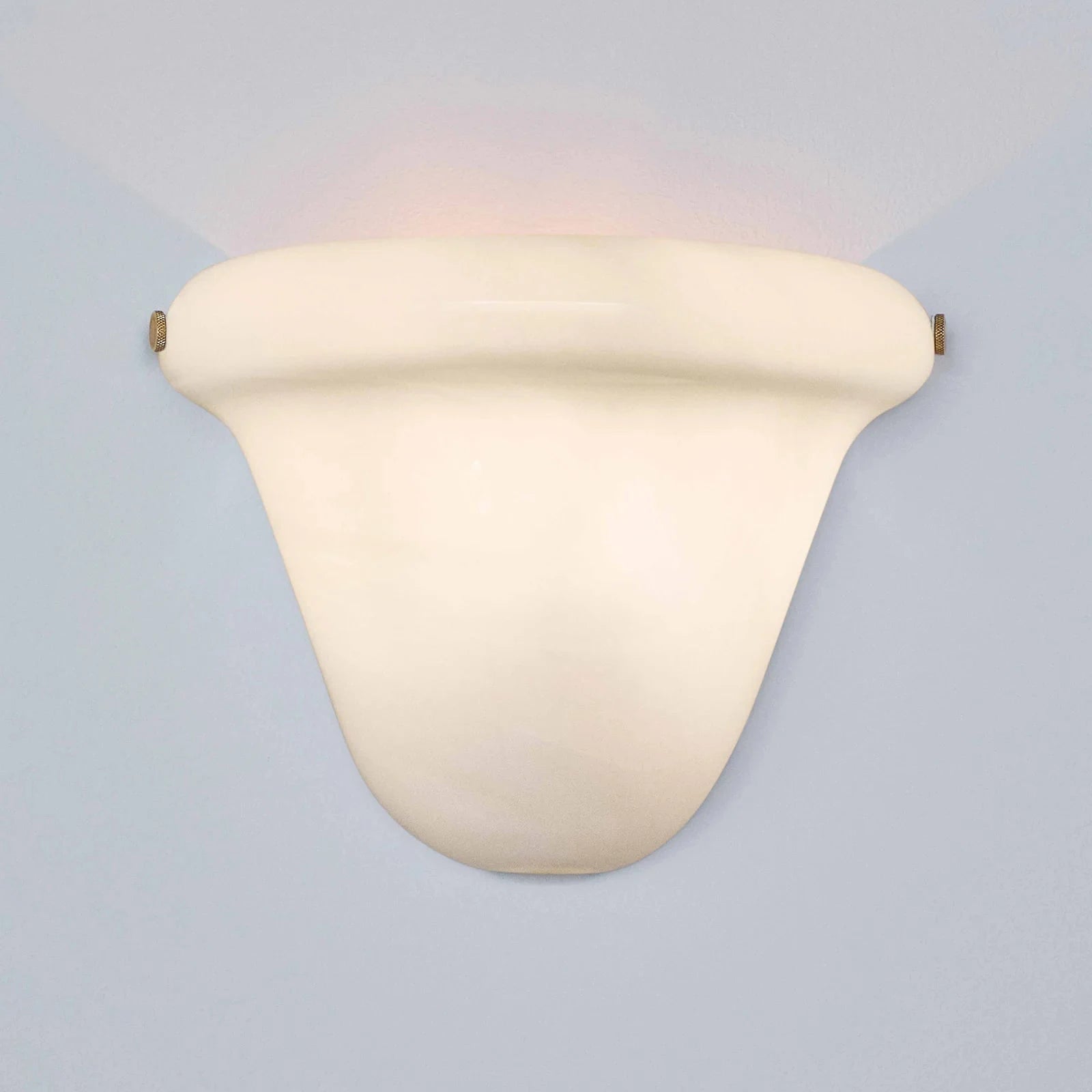 A modern wall-mounted sconce with a curved, shield-like shade in a warm cream or off-white finish, casting a soft warm light upward and downward against a pale blue-gray background.