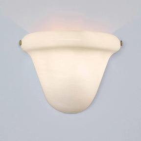 A modern wall-mounted sconce with a curved, shield-like shade in a warm cream or off-white finish, casting a soft warm light upward and downward against a pale blue-gray background.