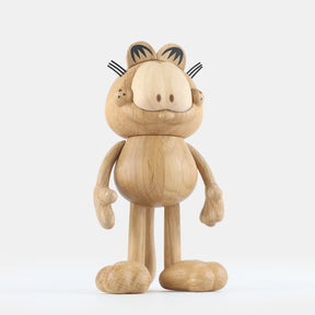 Wooden figurine of an animated cartoon cat character carved from light oak, featuring a rounded head with engraved facial details, stylized ears with black markings, short whisker lines, a rounded sculpted body, simplified limbs, visible natural wood grain, and a matte surface on a plain white background.