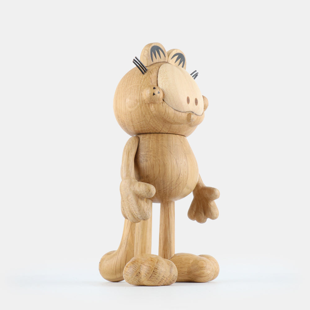 Wooden figurine of an animated cartoon cat character carved from light oak, featuring a rounded head with engraved facial details, stylized ears with black markings, short whisker lines, a rounded sculpted body, simplified limbs, visible natural wood grain, and a matte surface on a plain white background.