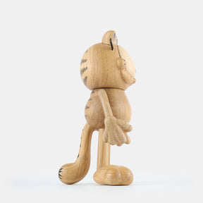 Side view wooden figurine of an animated cartoon cat character carved from light oak, featuring a rounded head with engraved facial details, stylized ears with black markings, short whisker lines, a rounded sculpted body, simplified limbs, visible natural wood grain, and a matte surface on a plain white background.