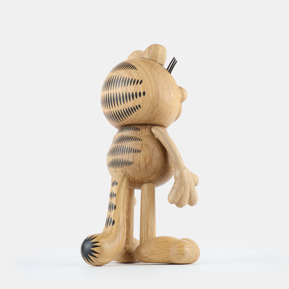 Wooden figurine of an animated cartoon cat character carved from light oak, featuring engraved black stripe patterns on the head, body, and tail, rounded sculpted limbs, visible natural wood grain, and a matte surface on a plain white background.