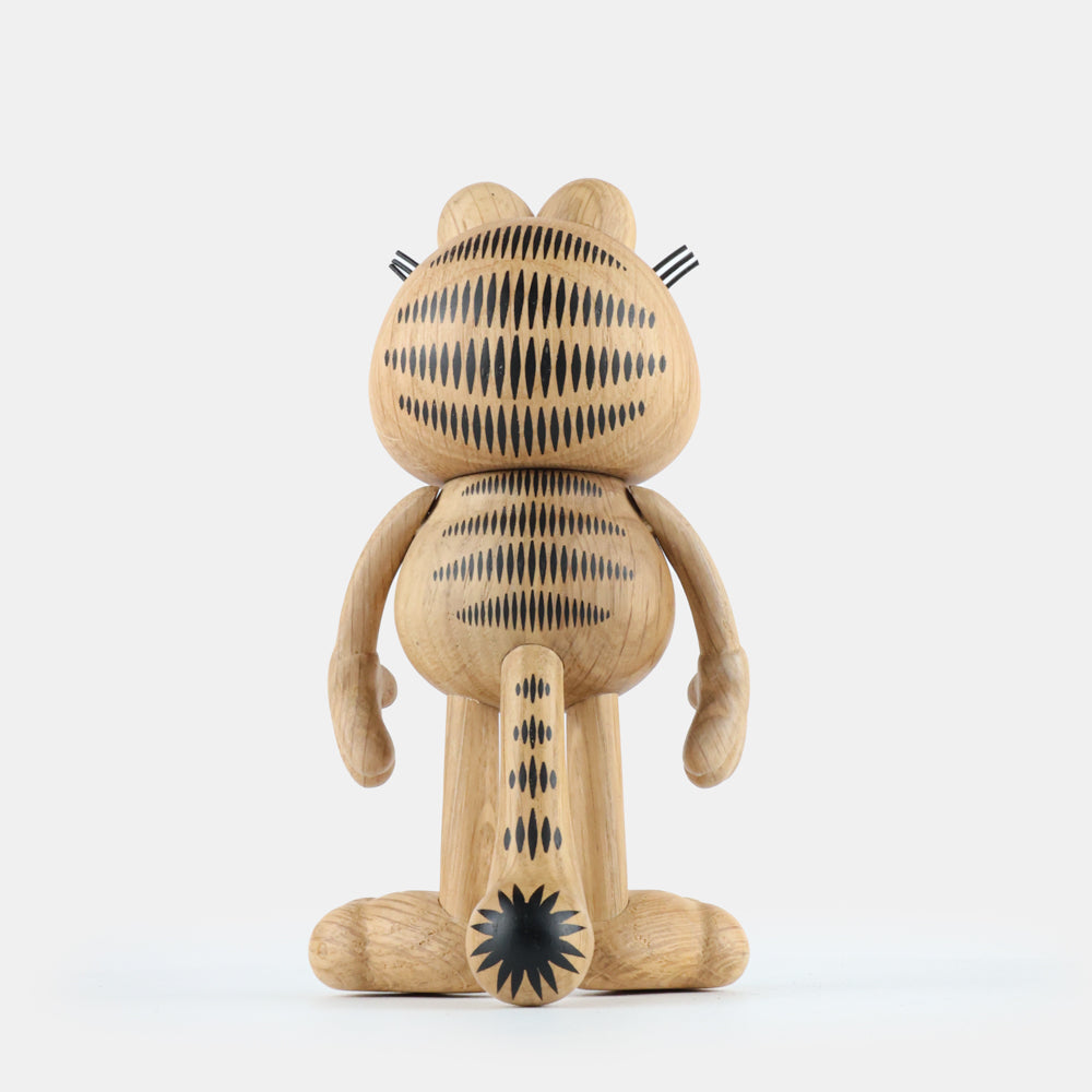 Back view of a wooden figurine of an animated cartoon cat character carved from light oak, featuring engraved black stripe patterns across the head, body, and tail, rounded sculpted limbs, visible natural wood grain, and a matte surface on a plain white background.