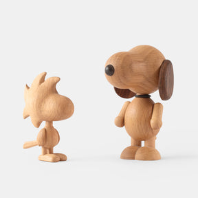 Two wooden figurines of animated cartoon characters carved from light oak, featuring rounded heads, stylized hair and ear shapes, simplified bodies and limbs, visible natural wood grain, and smooth matte surfaces on a plain white background.