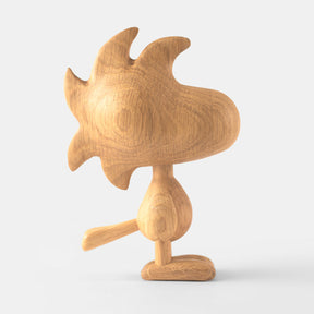 Wooden figurine of an animated cartoon character carved from light oak, featuring a rounded head with stylized protruding shapes, simplified body and tail, visible natural wood grain, and a smooth matte surface on a plain white background.