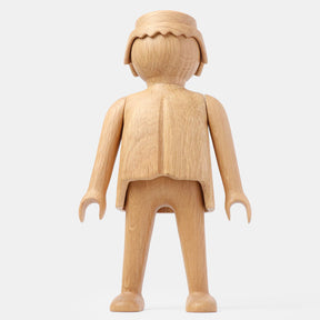 Front view of a finished wooden Playmobil-style human figure crafted from light oak, featuring a smooth rounded head with carved hair detail, simplified arms and legs, visible natural wood grain, and a clean matte finish on a plain white background.