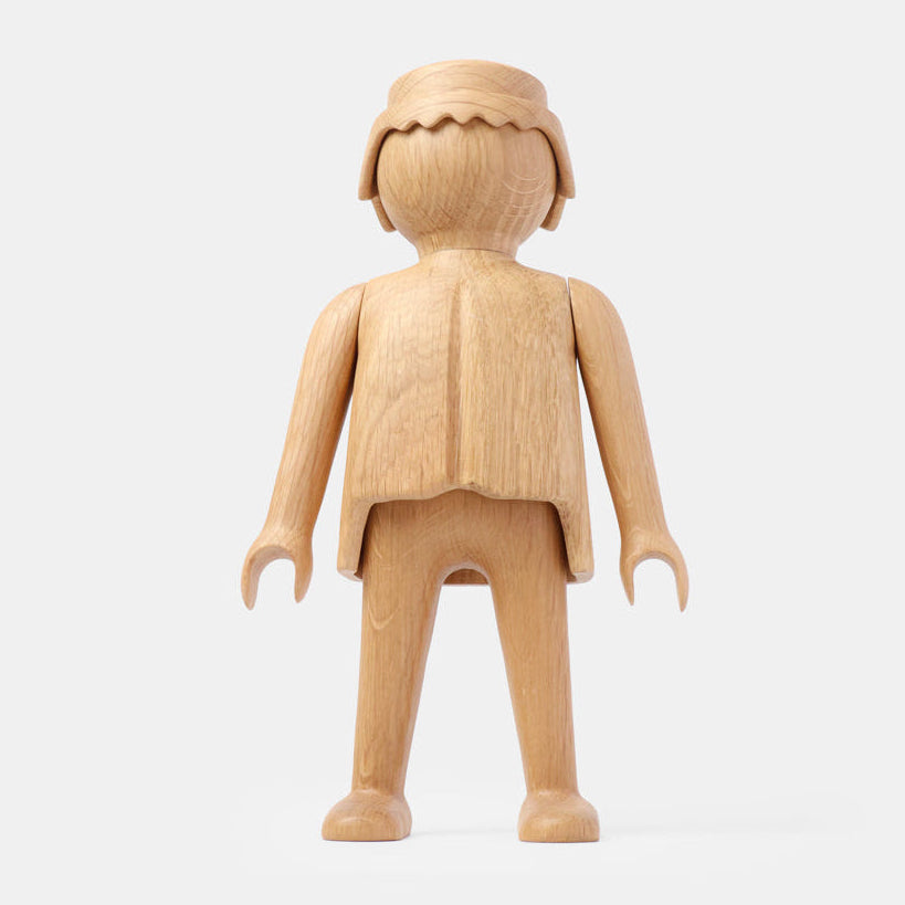 Front view of a finished wooden Playmobil-style human figure crafted from light oak, featuring a smooth rounded head with carved hair detail, simplified arms and legs, visible natural wood grain, and a clean matte finish on a plain white background.