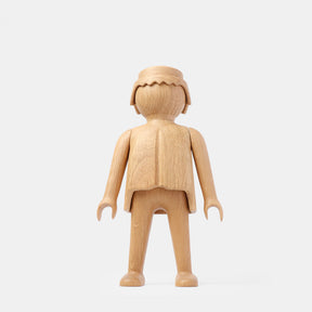 Front view of a finished wooden Playmobil-style human figure crafted from light oak, featuring a smooth rounded head with carved hair detail, simplified arms and legs, visible natural wood grain, and a clean matte finish on a plain white background.