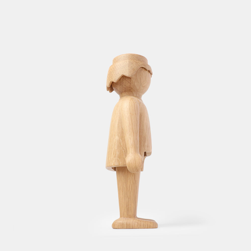 Wooden Playmobil-style human figure crafted from light oak, showing simplified proportions, a rounded head with carved hair detail, smooth sculpted arms and legs, visible natural wood grain, and a matte surface on a plain white background.
