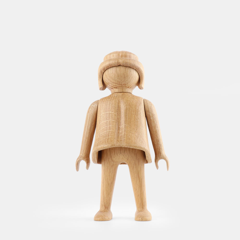 Wooden Playmobil-style girl figure made from light oak, featuring simplified proportions, a rounded head with carved hair detail, smooth sculpted arms and legs, visible natural wood grain, and a matte surface on a plain white background.