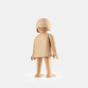 Wooden Playmobil-style girl figure made from light oak, featuring simplified proportions, a rounded head with carved hair detail, smooth sculpted arms and legs, visible natural wood grain, and a matte surface on a plain white background.