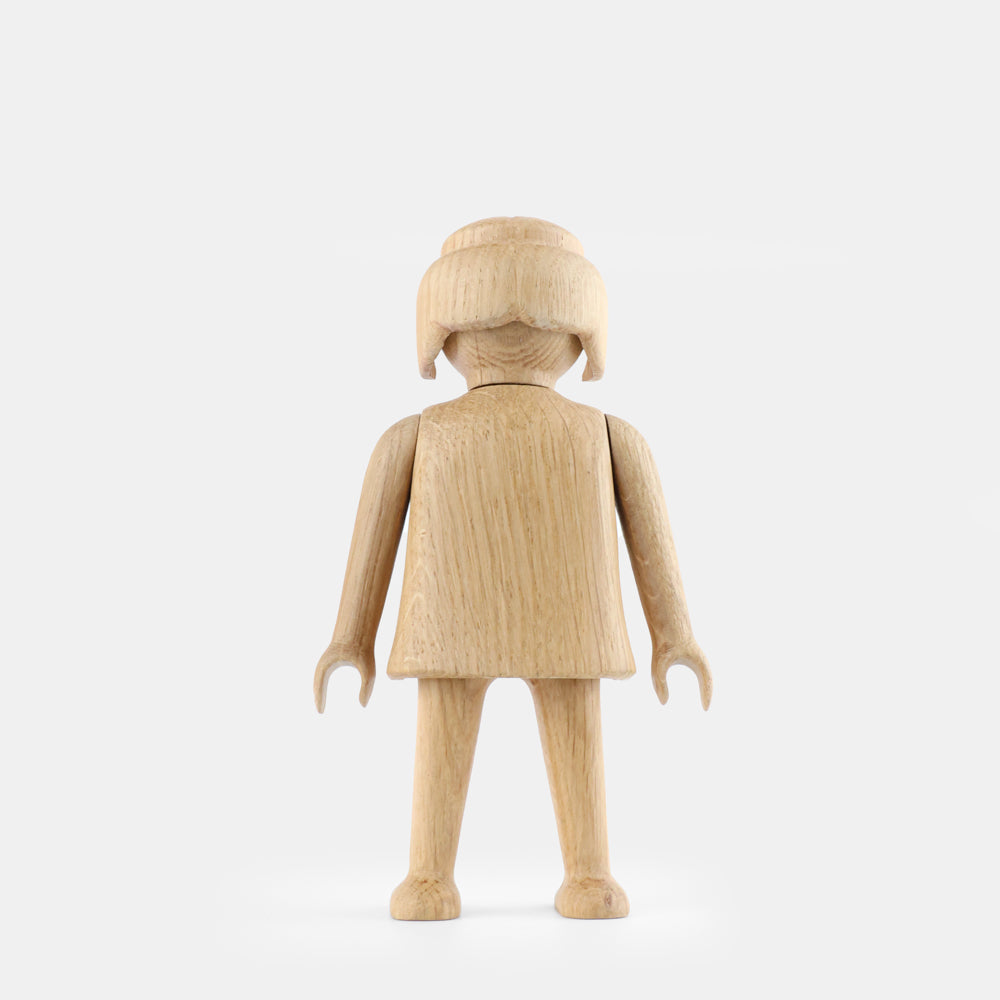 Wooden Playmobil-style girl figure made from light oak, featuring simplified proportions, a rounded head with carved hair detail, smooth sculpted arms and legs, visible natural wood grain, and a matte surface on a plain white background.