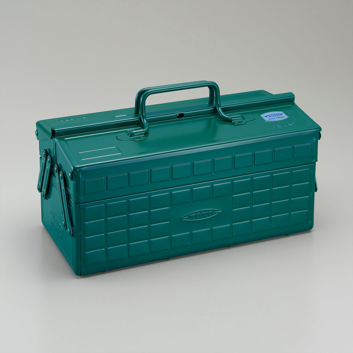 Antique green Toyo steel cantilever toolbox, closed, three-quarter view showing embossed grid panels, folded side arms, and integrated top carry handle.