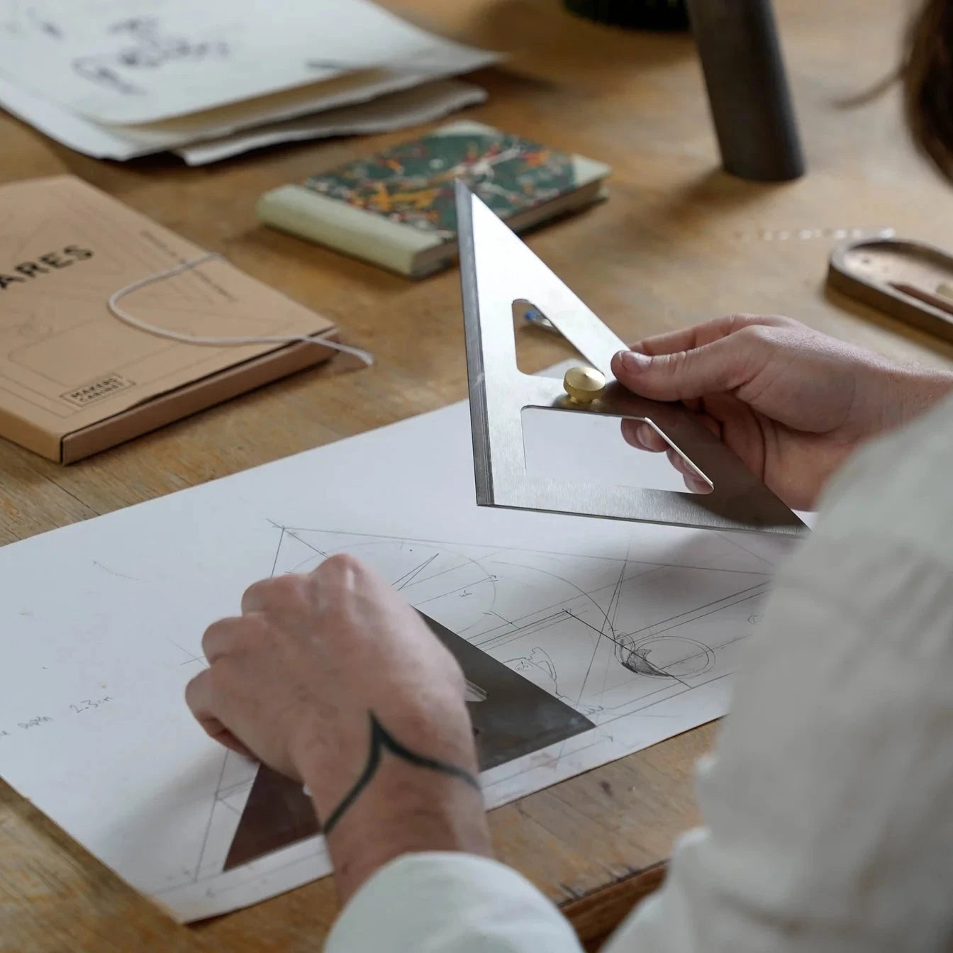 Person using a protractor on a piece of paper with architectural drawings on a wooden table.