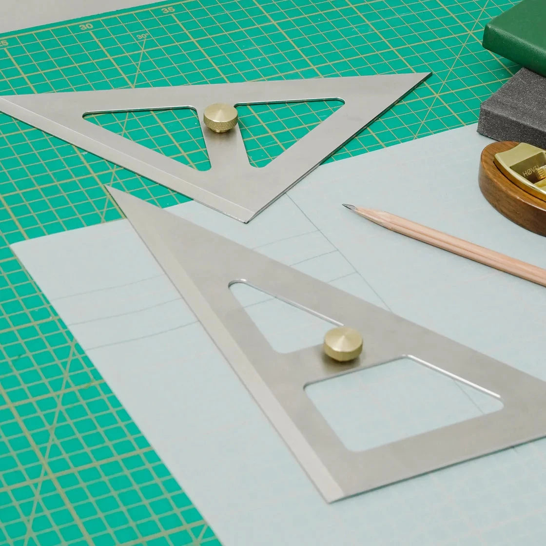 Two metal speed triangles on a cutting mat with a pencil and eraser.