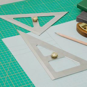 Two metal speed triangles on a cutting mat with a pencil and eraser.