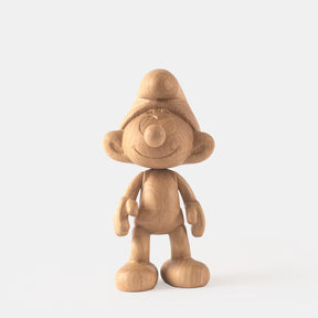 Wooden figurine of a small animated cartoon character, carved from light oak, featuring a rounded hat, smiling facial details, simplified body proportions, visible natural wood grain, and a smooth matte surface on a plain white background.
