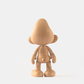 Wooden figurine of a small animated cartoon character seen from behind, carved from light oak, featuring a rounded hat, simplified limbs and body, visible natural wood grain, and a smooth matte surface on a plain white background.