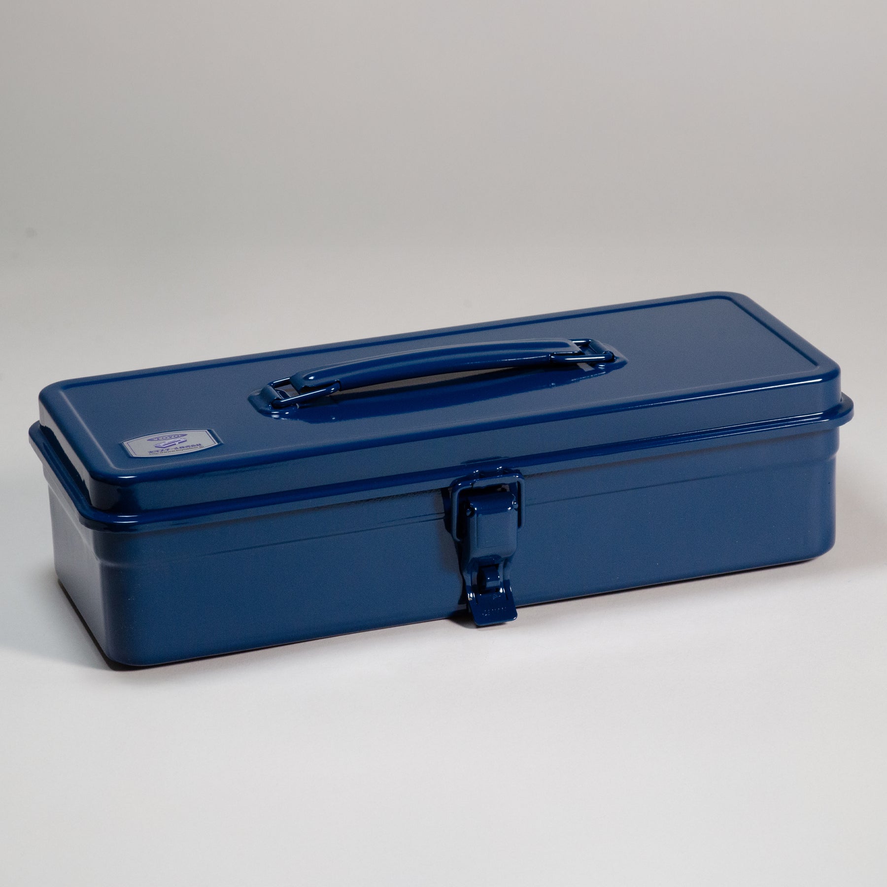 Indigo Toyo Steel metal toolbox with a glossy enamel finish, long rectangular profile, top-mounted carry handle, and single front latch, photographed closed against a neutral studio background.