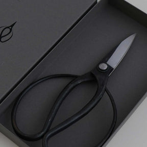 Black-handled scissors with silver metal blades, presented inside a dark gray gift box.
