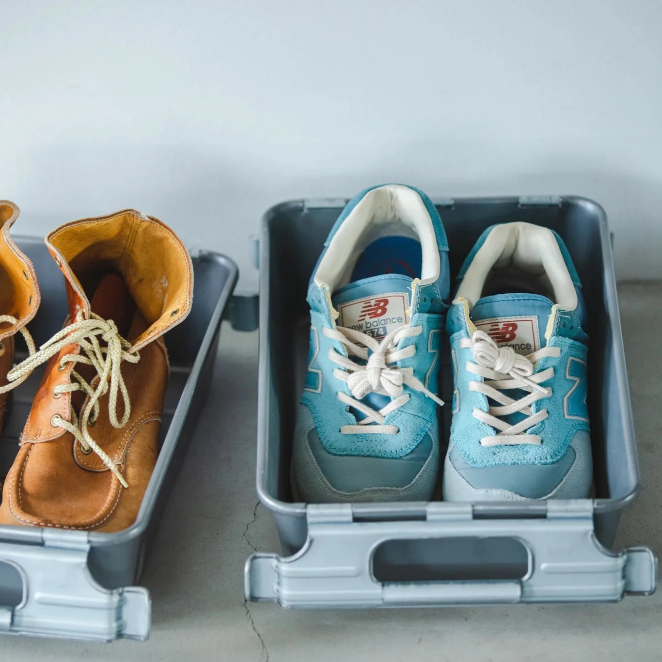 Metal storage bins used as shoe organizers, holding a pair of blue sneakers and brown leather boots.