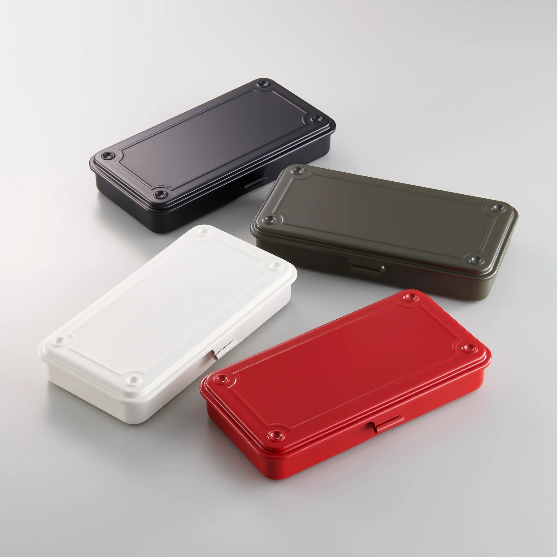 Four rectangular metal storage boxes with lids in black, olive green, white, and red, arranged on a light background.