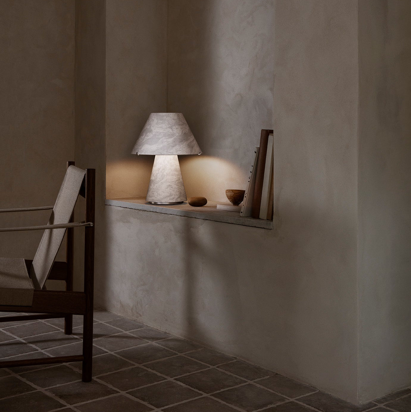 Lamp on a shelf in a dimly lit room with textured walls and tiled floor.