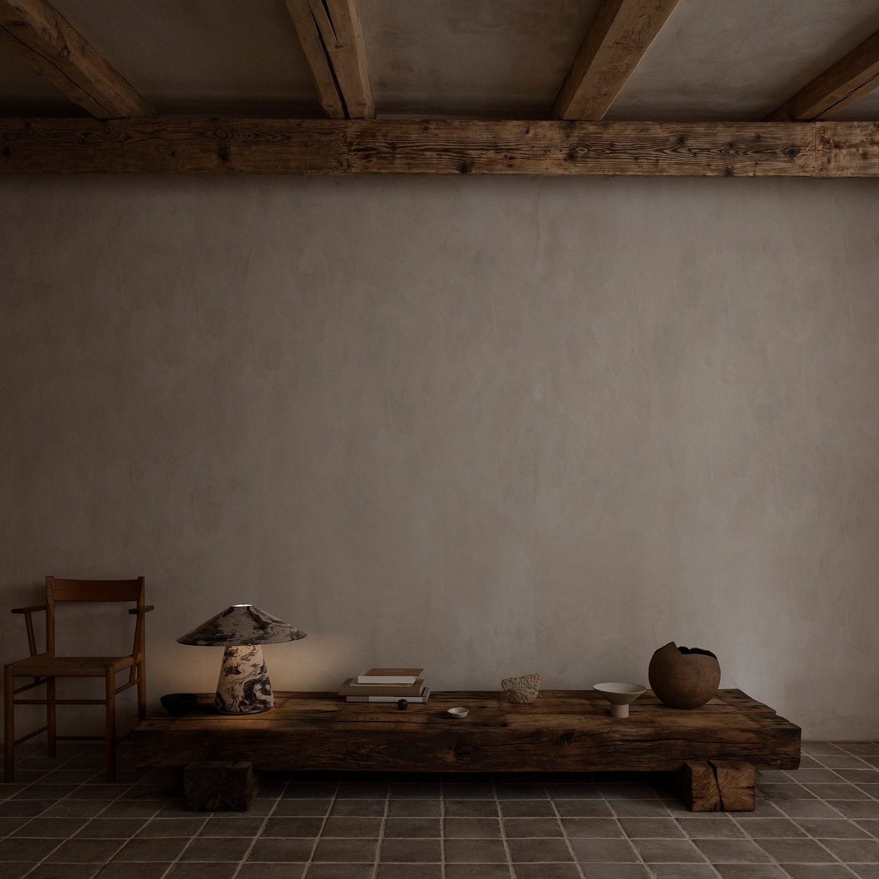 Simple interior with a wooden table, chair, and decorative items against a plain wall.