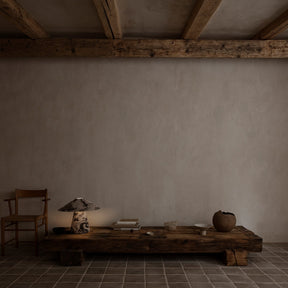 Simple interior with a wooden table, chair, and decorative items against a plain wall.