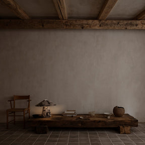 Simple interior with a wooden table, chair, and decorative items against a plain wall.