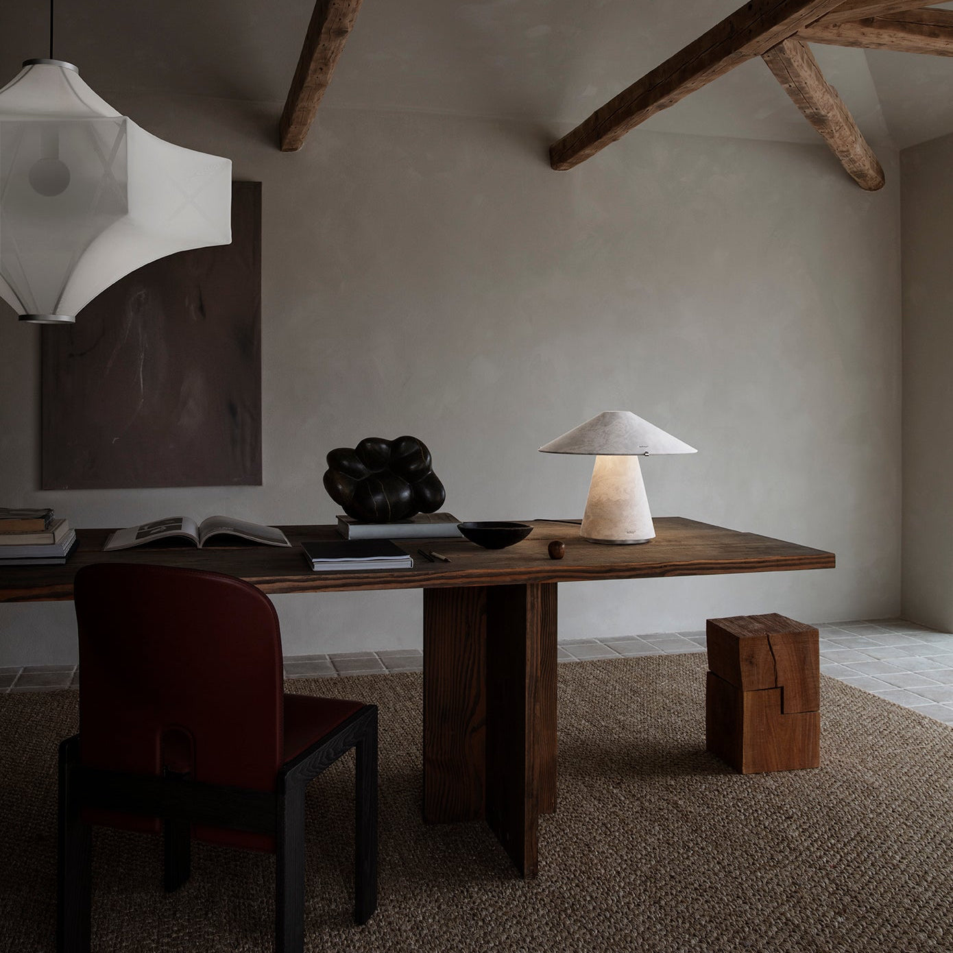 Modern interior with wooden desk, chair, and lamp in a room with exposed beams.