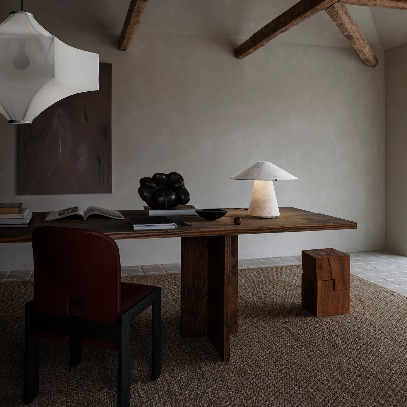 Modern interior with wooden desk, chair, and lamp in a room with exposed beams.