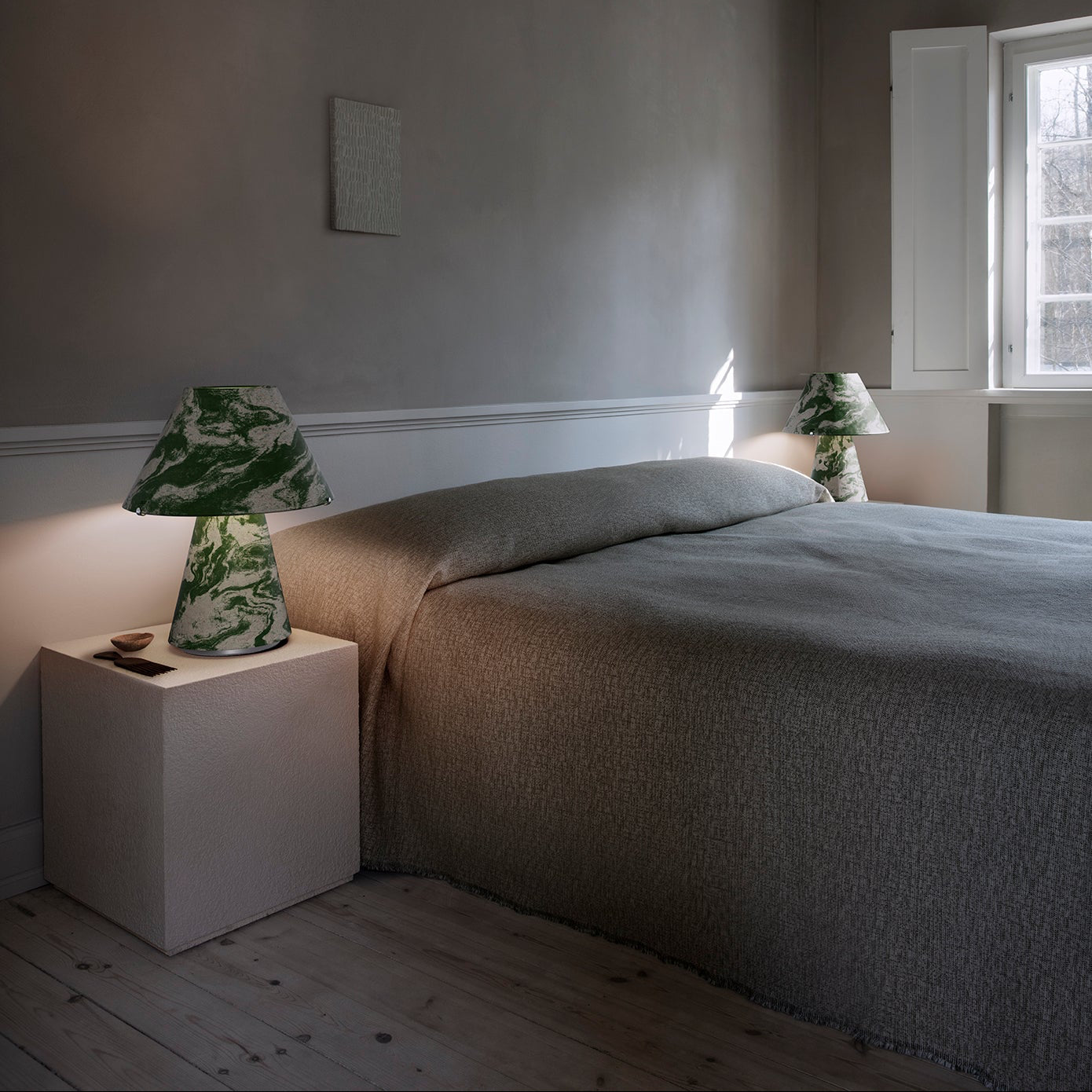 Minimalist bedroom with a bed, nightstands, and lamps against a plain wall.