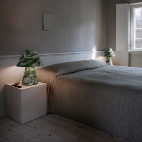 Minimalist bedroom with a bed, nightstands, and lamps against a plain wall.