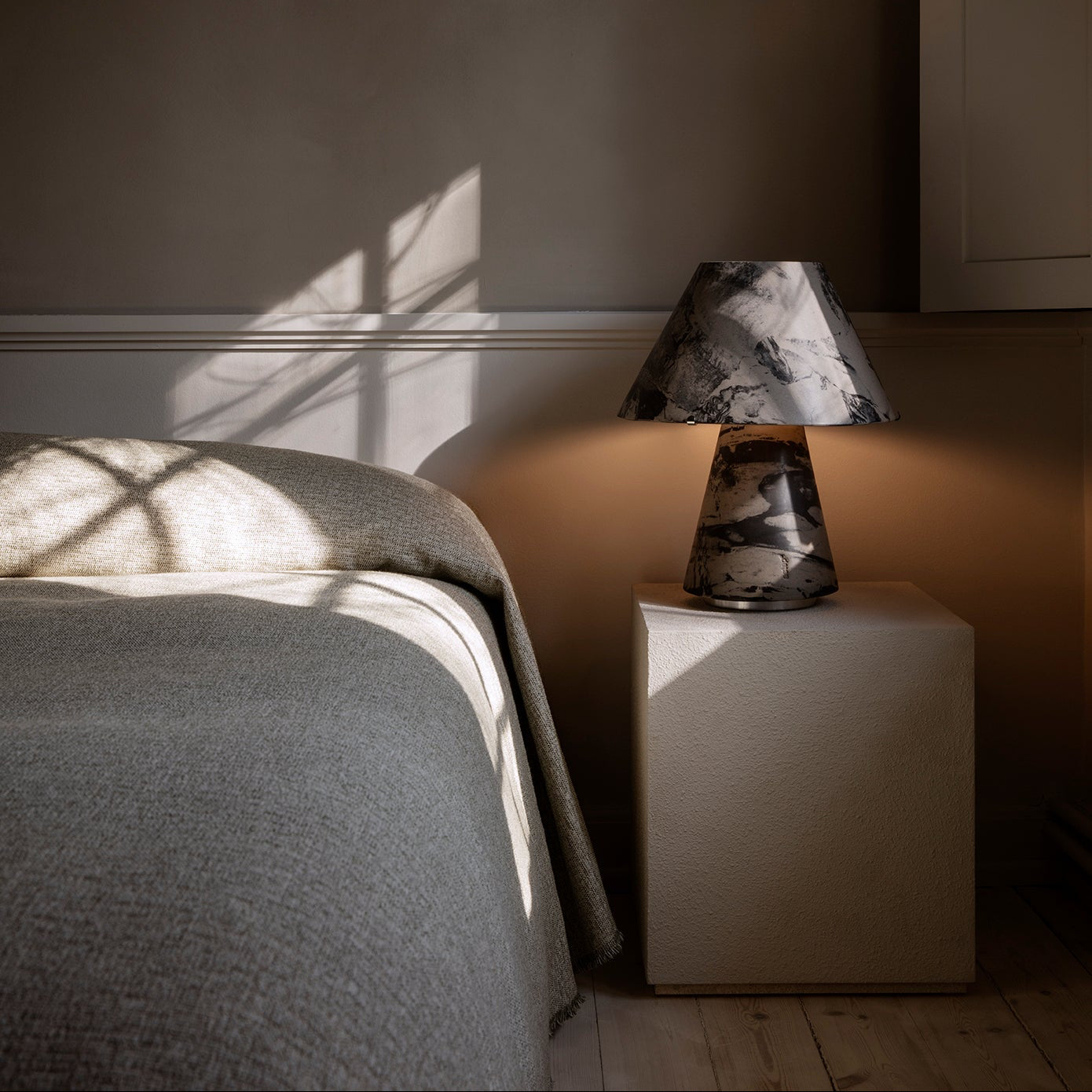 Bedroom scene with a bed and nightstand featuring a lamp against a dark wall.