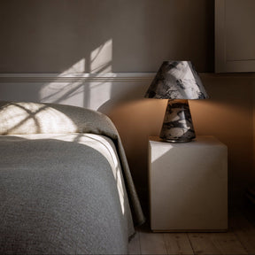 Bedroom scene with a bed and nightstand featuring a lamp against a dark wall.