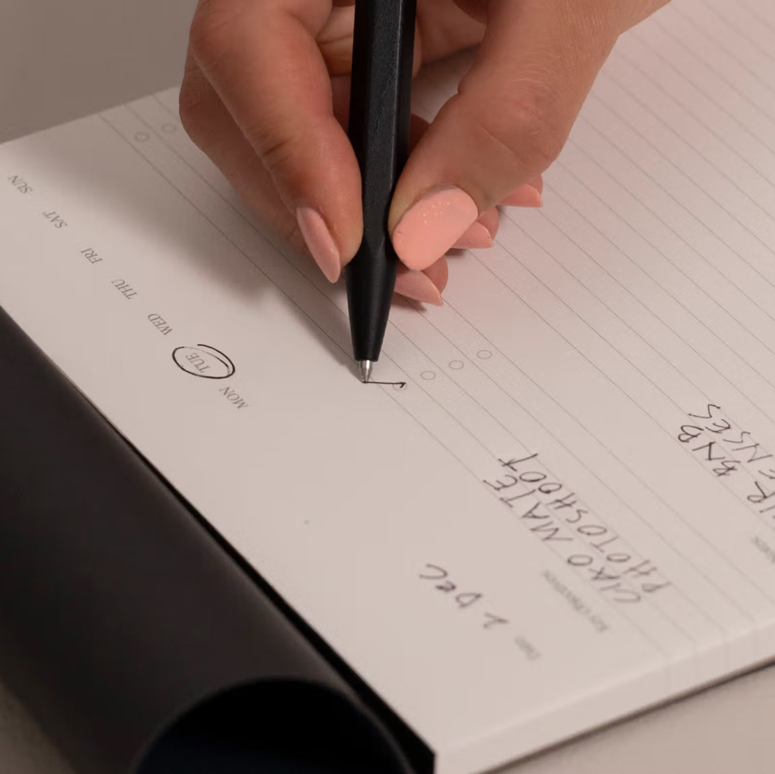 Hand holding a pen over a notebook with writing on a light background