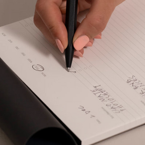 Hand holding a pen over a notebook with writing on a light background