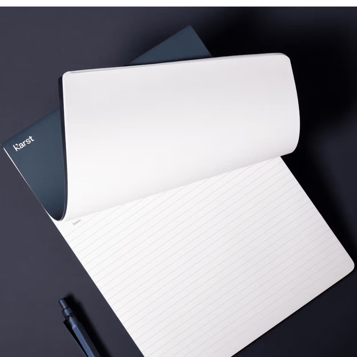 White notebook with a pen on a dark surface