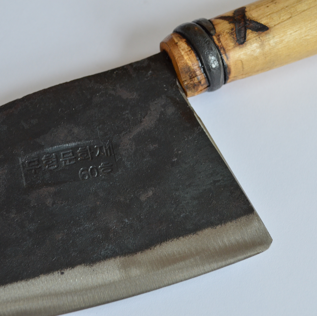 Close-up of a hand-forged chef’s knife with a dark patina steel blade and light wooden handle, shown on a clean white background to highlight artisan craftsmanship and blade detail.