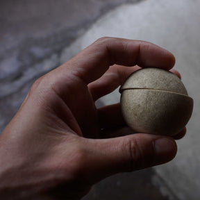 Hand holding a small stone ball against a blurred background