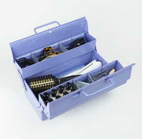 Toyo ST-350 steel cantilever toolbox in lilac, open with trays extended and filled with beauty tools including hairbrushes, clips, bottles, and styling accessories on a white background.