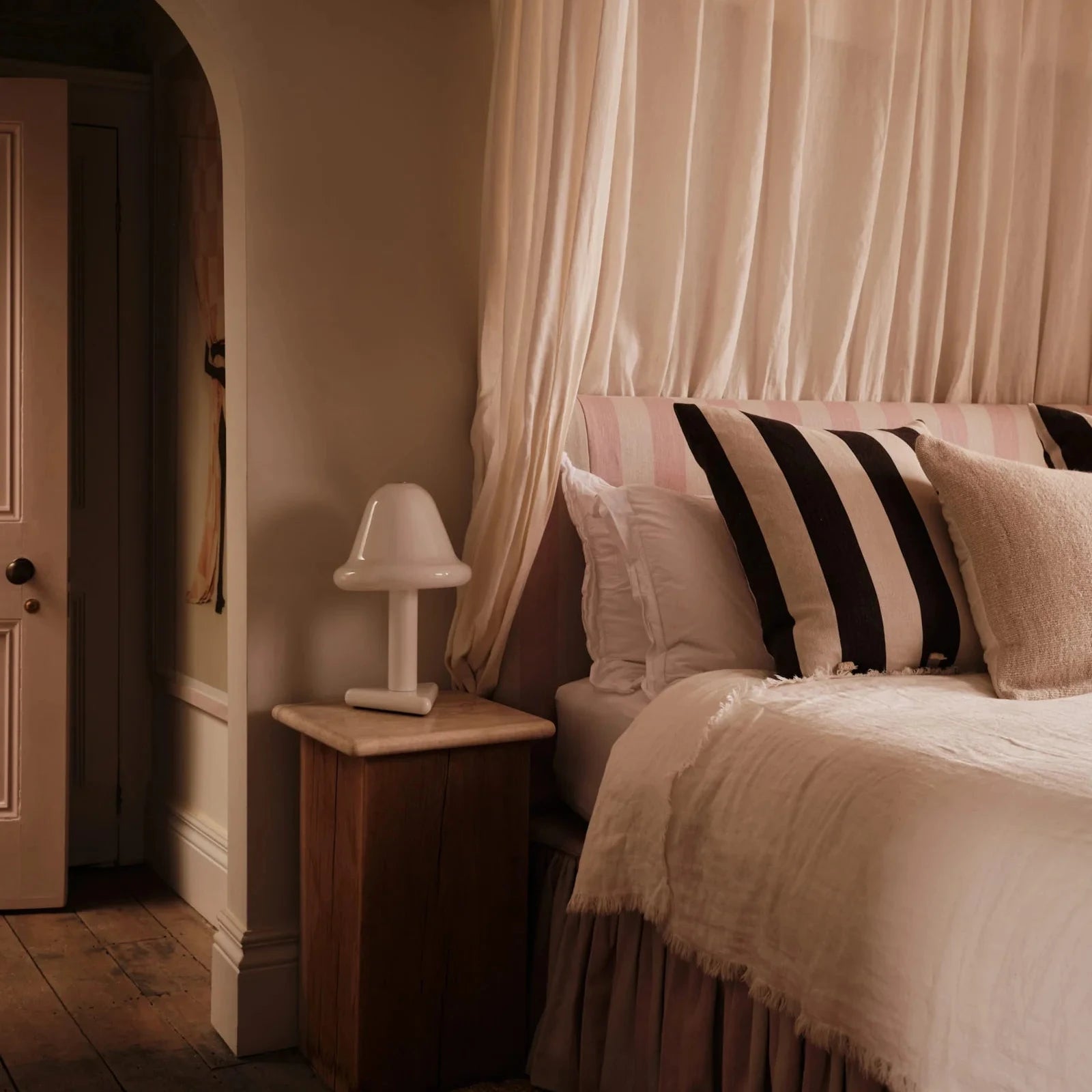 Bedroom with a canopy bed and striped pillows, featuring a lamp on a nightstand.
