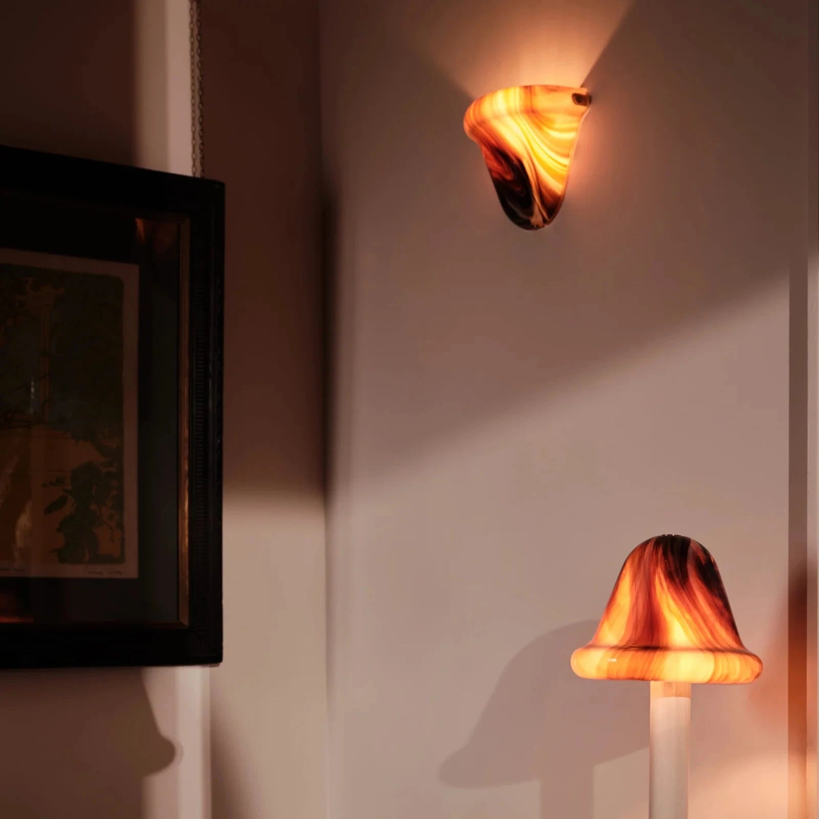 A warm glowing mushroom-shaped wall sconce mounted on a wall above a striped armchair, with a matching floor lamp below.