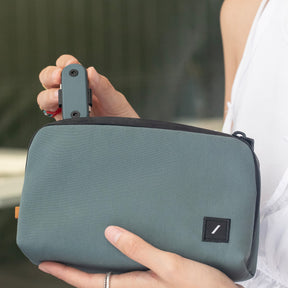 Person holding a green travel pouch with a keychain attached, blurred background