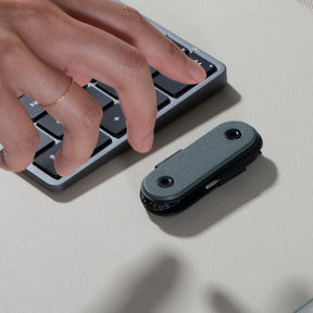 Hand using a mechanical keyboard with a small black device on a light surface