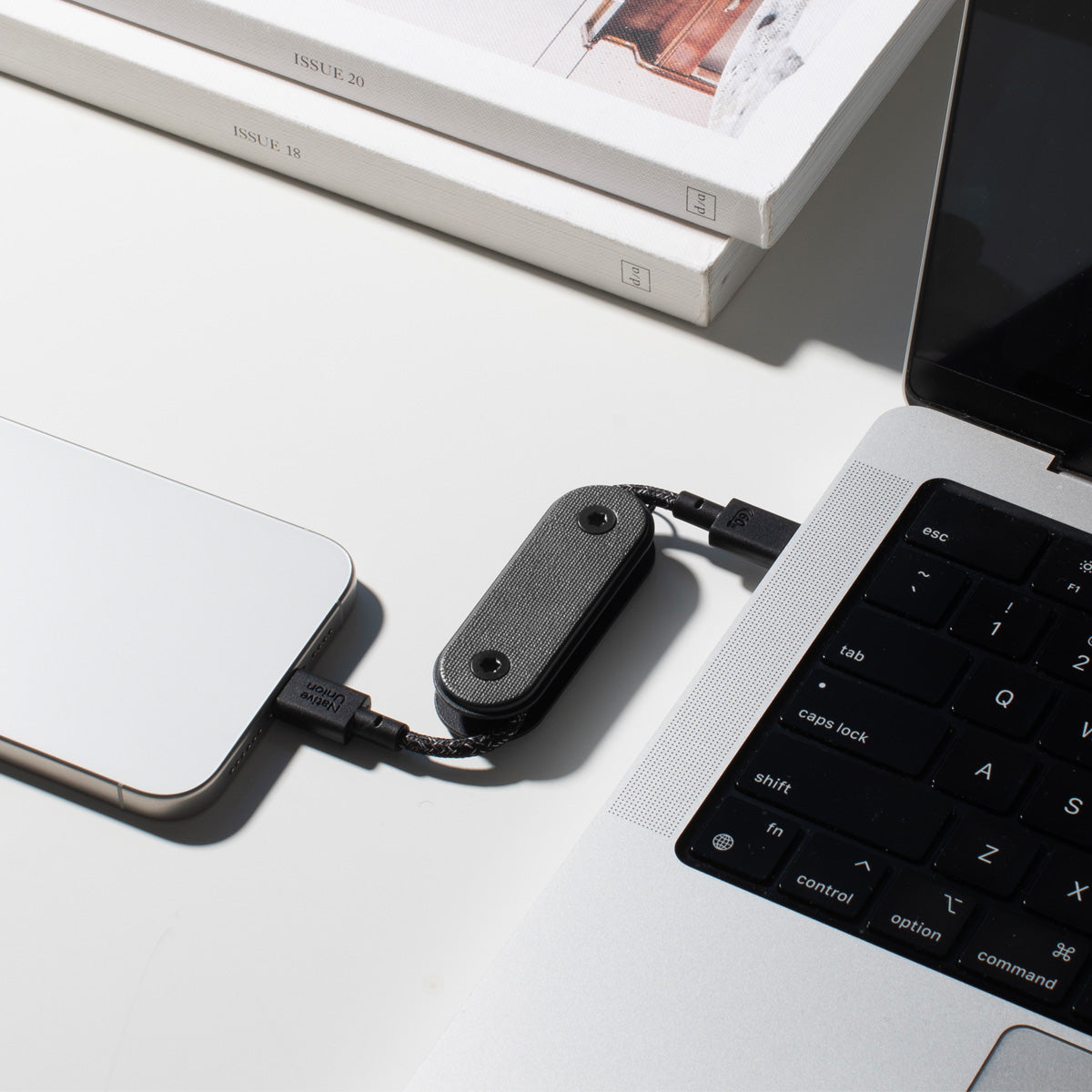 Small black device connected to a laptop and phone on a light surface