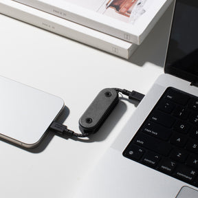 Small black device connected to a laptop and phone on a light surface